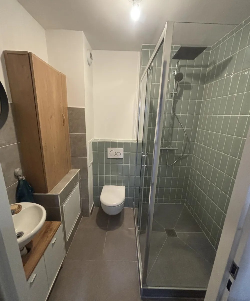 Salle de bain rénovée : douche vitrée carrelée en vert, WC suspendu et meuble vasque